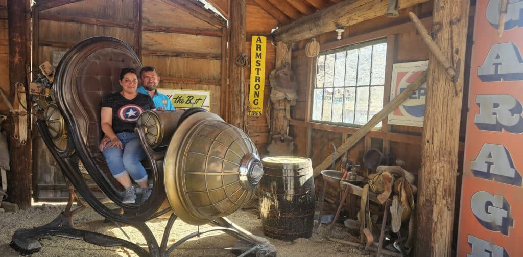 A couple relaxes on a futuristic chair in a rustic Nevada garage, perfect for Las Vegas ghost town tours or ATV adventures nearby.