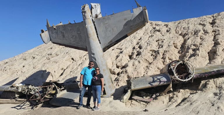 Smiling couple poses by a historic airplane wreck near Las Vegas, Nevada—perfect for ATV tours and Ghost Town sightseeing.