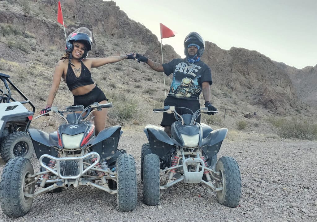 Smiling riders hold hands on ATVs in Nevada’s desert near Las Vegas, enjoying an ATV tour by the Colorado River.