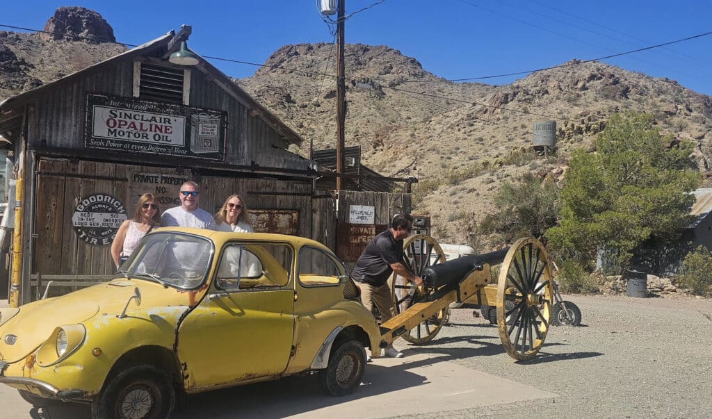 Group poses by a vintage yellow car and cannon at a Nevada ghost town near Las Vegas—perfect for ATV tours and RZR rides!.