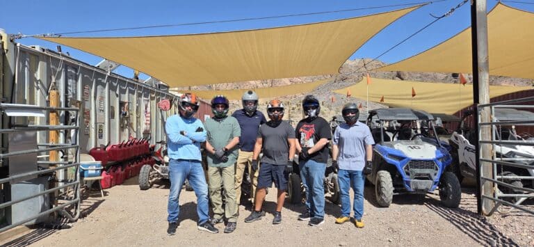 Six adventurers in helmets gear up for Nevada ATV tours near Las Vegas, with RZR rides and Colorado River views in the background.
