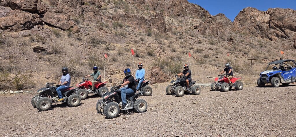 Group riding ATVs near a Nevada mountainside on a Las Vegas ATV tour, with RZR off-road vehicle by the Colorado River.