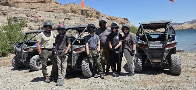Adventure seekers in helmets and gloves pose by ATVs near the Colorado River, ready for a Las Vegas RZR off-road tour in Nevada.