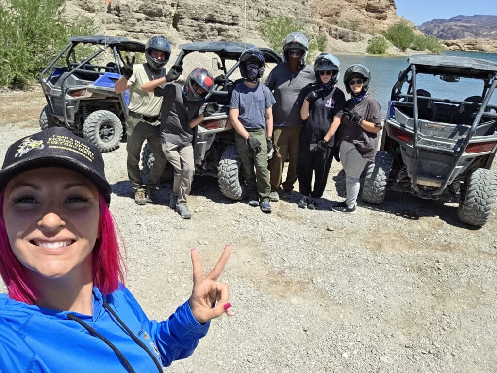 Smiling woman with pink hair snaps selfie by friends, ATVs & Colorado River in Nevada desert near Las Vegas on RZR tour.