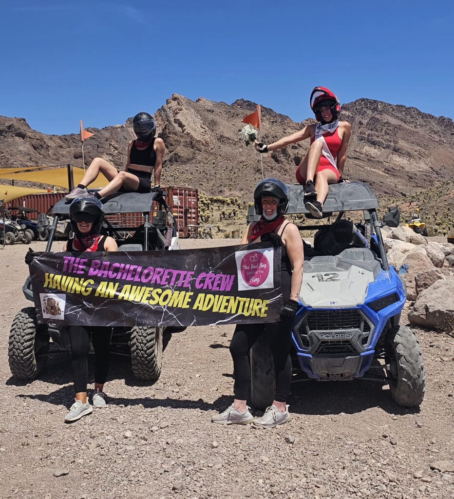 Four women in helmets celebrate a Las Vegas bachelorette with RZR off-road rides in Nevada desert near the Colorado River.