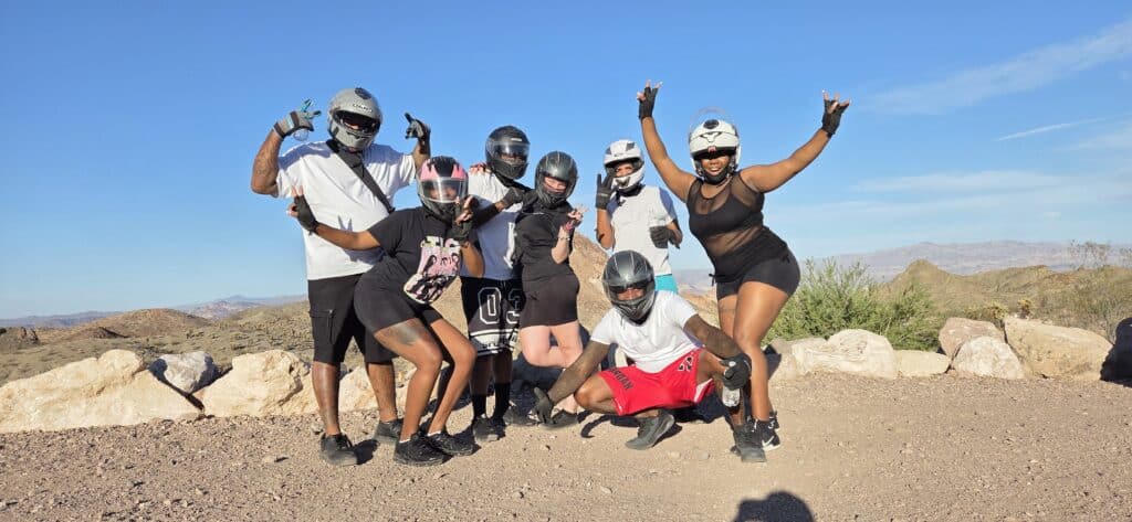 Seven friends in helmets and sporty gear pose on a rocky Nevada trail after an epic Las Vegas ATV tour by the Colorado River.