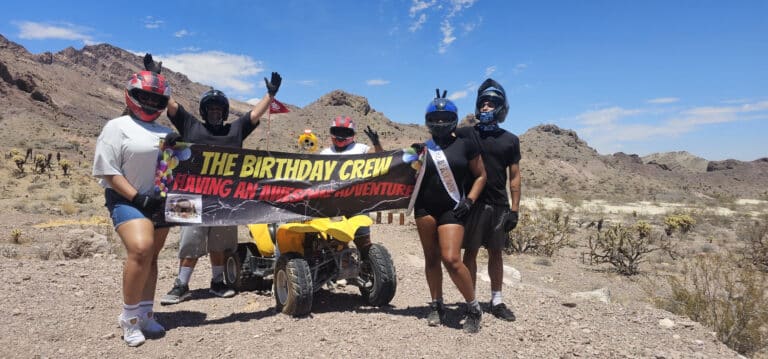 Five friends in helmets pose with a yellow ATV in the Nevada desert near Las Vegas during an epic Colorado River ATV tour.