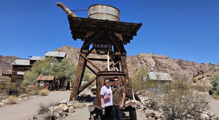 Two people by a vintage Hamms Beer water tower and classic truck in a Nevada ghost town near Las Vegas—perfect for ATV or RZR rides.