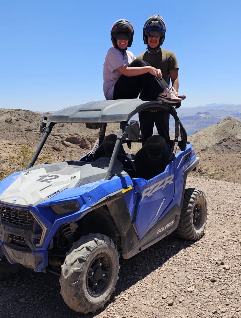 Two people in helmets with a blue Polaris RZR on a rocky Nevada desert trail near Las Vegas, perfect for ATV tours and off-road adventures.