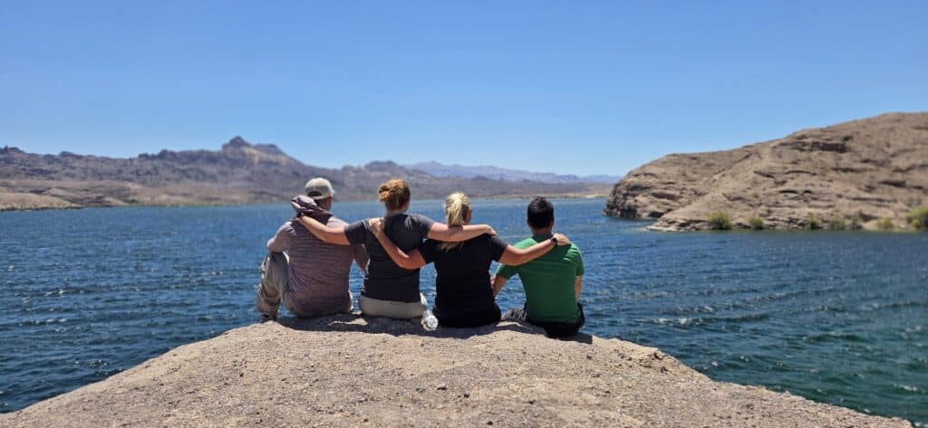 Four friends sit together on a rocky outcrop by the Colorado River near Las Vegas, Nevada, after an epic RZR off-road adventure.