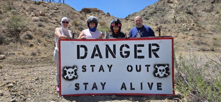 Four people by a DANGER STAY OUT sign near Las Vegas, Nevada desert—perfect for ATV tours & RZR off-road adventures!.