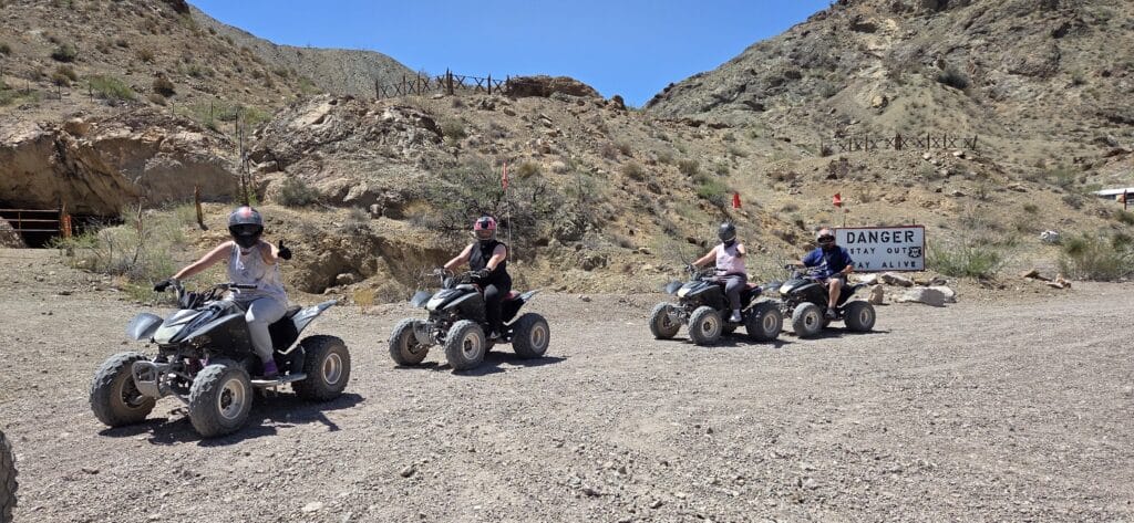 Adventure seekers ride ATVs on a rocky desert trail near Las Vegas, Nevada; DANGER sign warns along thrilling ATV tours and RZR rides.