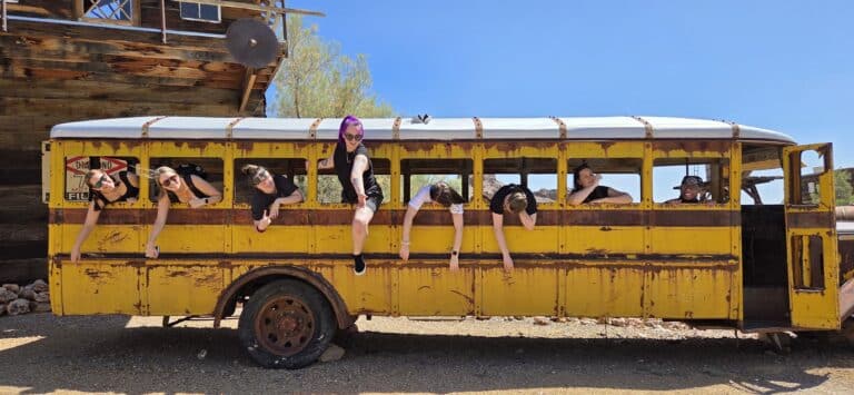 Seven in black lean from a vintage yellow school bus near a Nevada ghost town, ready for Las Vegas RZR off-road adventures.