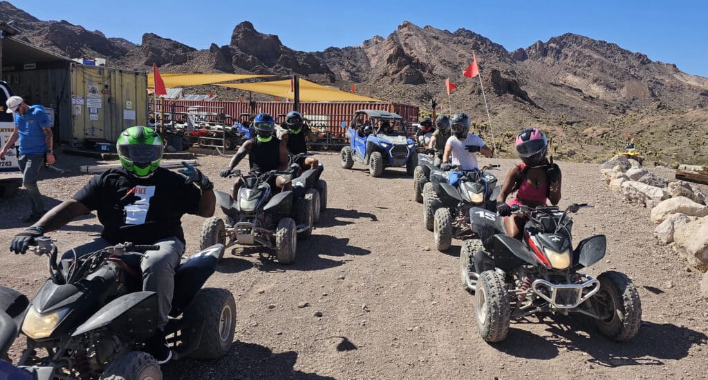 Adventurers in helmets enjoy an ATV tour near Las Vegas, Nevada, riding rocky trails with red flags and scenic mountain views.