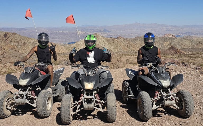Adventurers in helmets and masks pose on ATVs with red flags in the Nevada desert near Las Vegas on an exciting ATV tour.