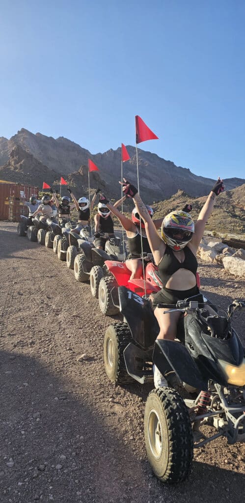 Adventurers in helmets ride ATVs with red flags on a Nevada dirt trail near Las Vegas, Rocky Mountains, and the Colorado River.