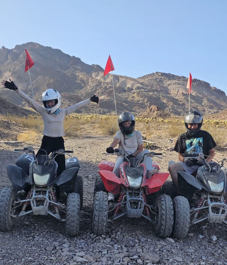 Riders in helmets enjoy an exciting ATV tour near Las Vegas, Nevada, with red flags waving against rocky desert mountains.