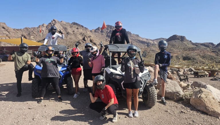 Adventurers in helmets enjoy an ATV tour near Las Vegas, Nevada, with RZRs on rocky desert terrain and mountain views.