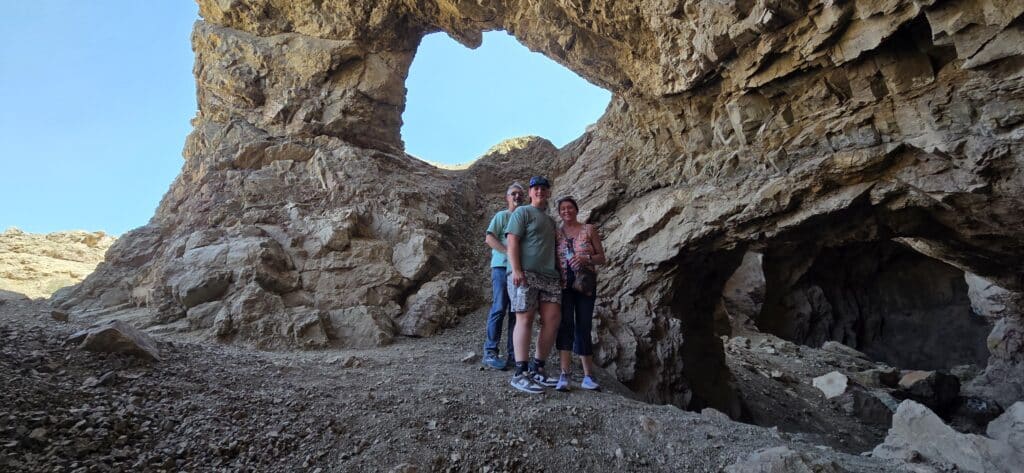 Three people pose by a rocky arch near Las Vegas, Nevada—perfect spot for ATV tours, RZR rides, and Colorado River views.