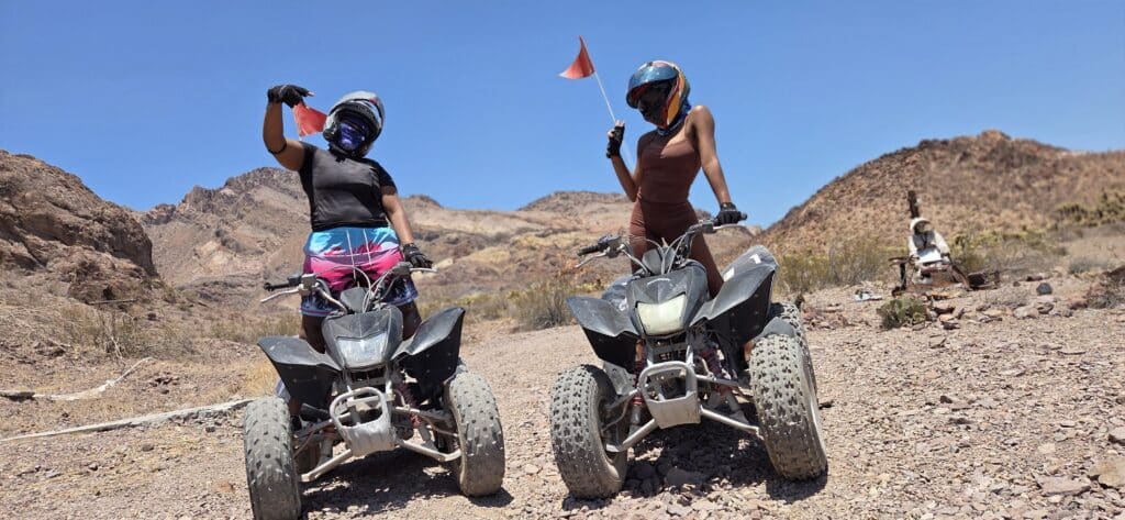 Riders wearing helmets enjoy an ATV tour near Las Vegas, Nevada, with red flags waving in the rocky desert by the Colorado River.