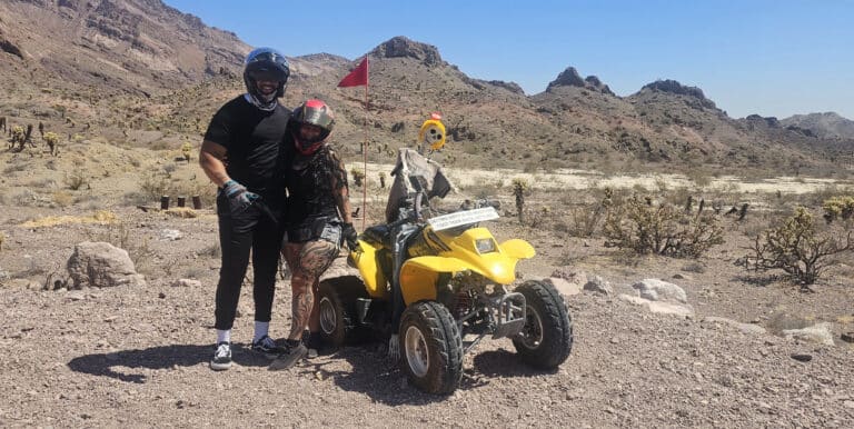 Two riders in helmets pause by a yellow ATV on a Nevada desert trail near Las Vegas, perfect for ATV tours and RZR off-road rides.
