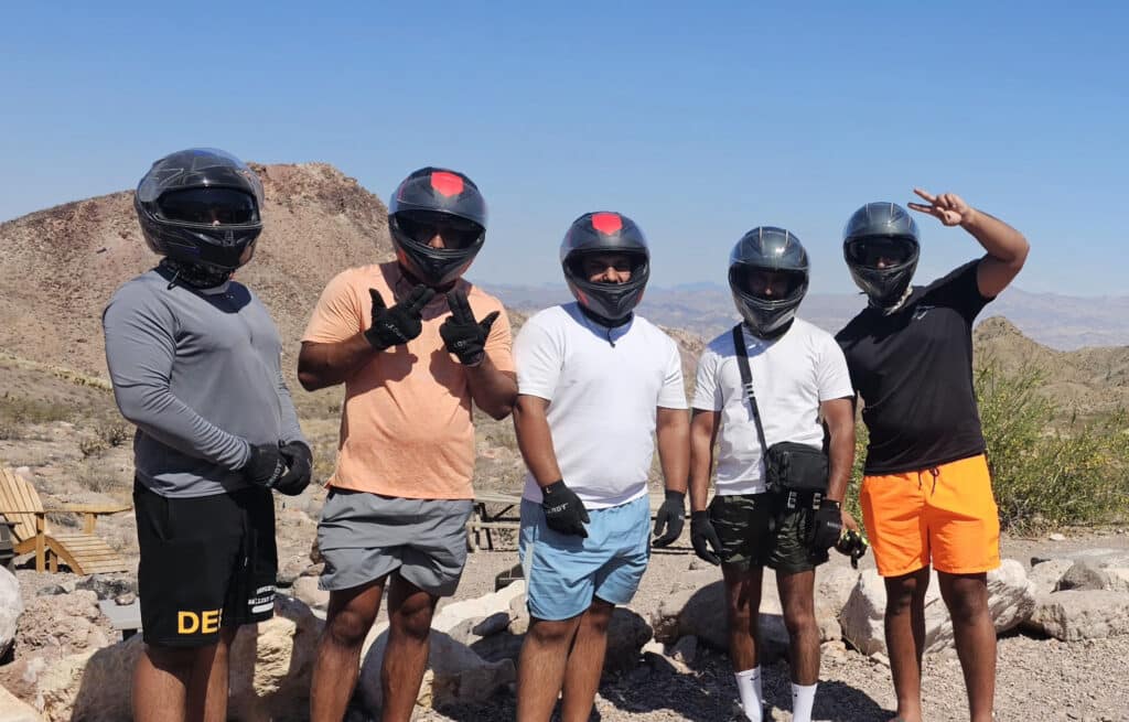 Group of five in helmets and activewear pose in Nevada desert near Las Vegas after an exciting RZR off-road ATV tour.