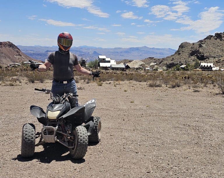 Adventurer in red helmet by black ATV on a Nevada desert plain near Las Vegas—perfect for ATV tours & Ghost Town sightseeing.
