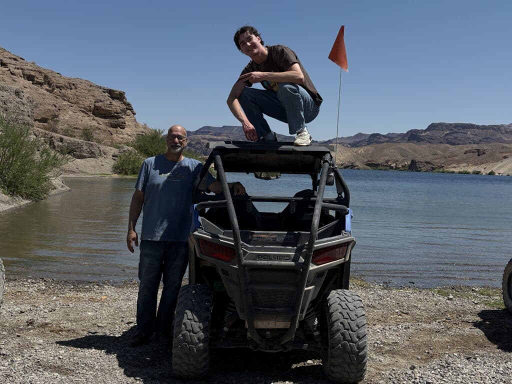 Two men pose with a Polaris RZR by the Colorado River near Las Vegas, Nevada—perfect spot for ATV tours and off-road adventures!.