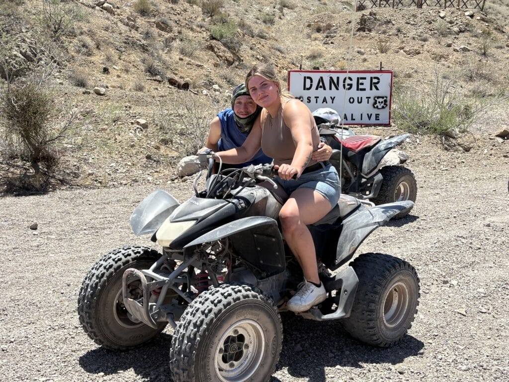 Two riders on an ATV pause by a Danger Stay Out sign in the Nevada desert near Las Vegas on an ATV tour adventure.