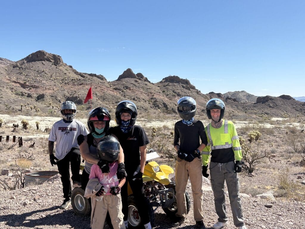 Group in helmets poses by yellow ATV in Nevada desert near Las Vegas, enjoying family-friendly ATV tours under clear blue skies.