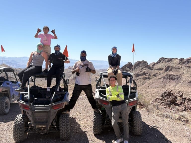 Six friends enjoy an ATV tour near Las Vegas, posing on RZRs amid Nevada’s desert rocks under a clear blue sky.