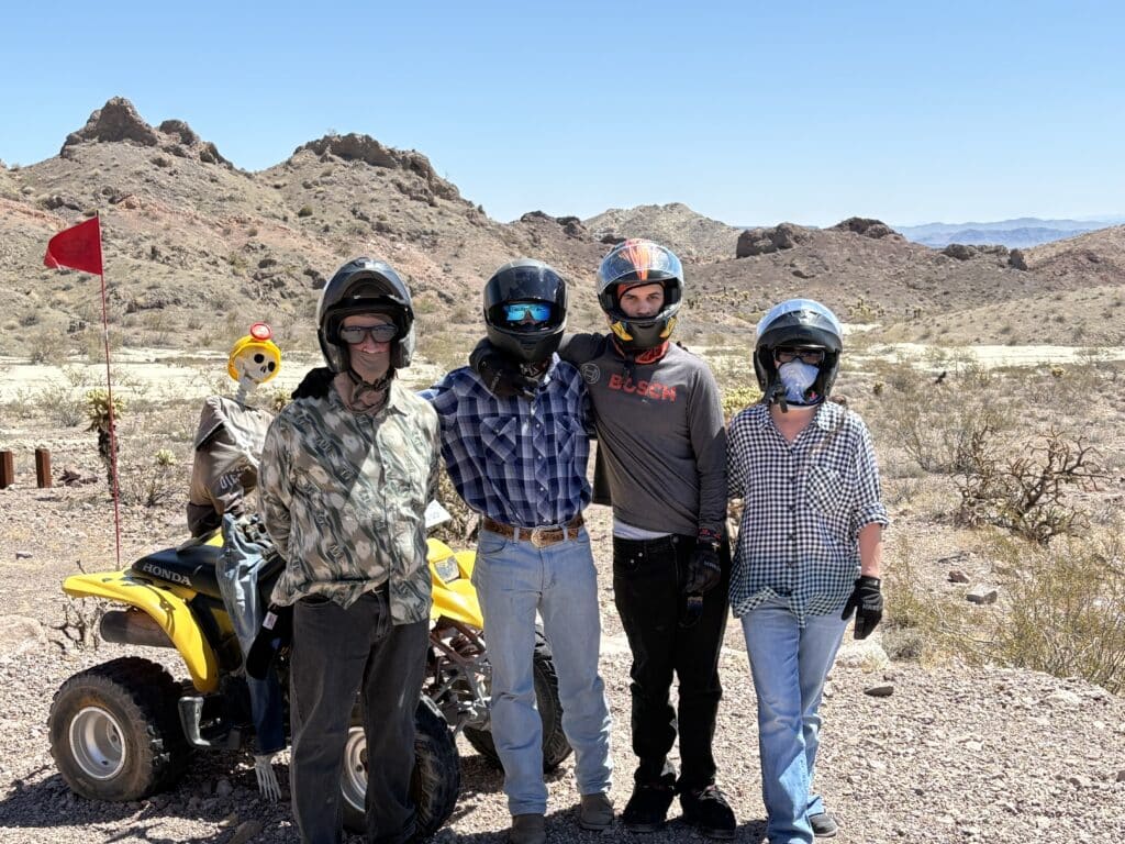 Group in helmets poses by a yellow ATV near Las Vegas, Nevada desert hills—perfect for RZR off-road rides and ATV tours.