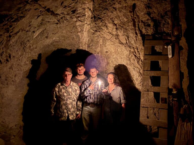 Four explore a dim Nevada mine near Las Vegas, candle-lit amid stone walls—perfect for ATV tours or Ghost Town sightseeing.