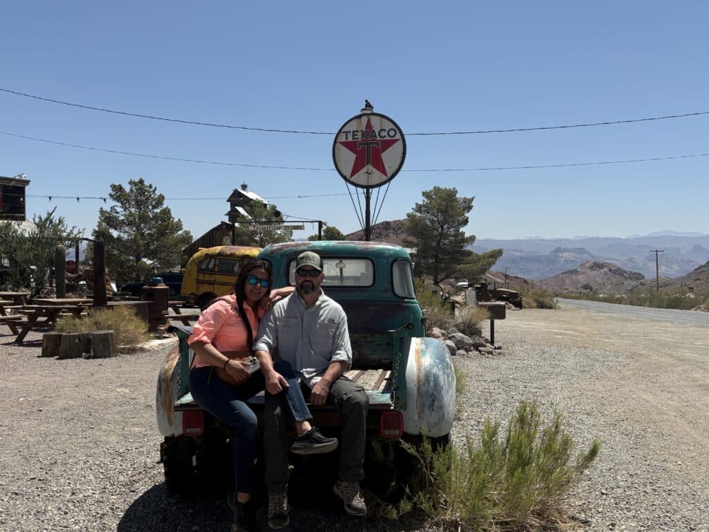 A couple relaxes on a vintage turquoise truck under a Texaco sign near Las Vegas, Nevada, perfect for Ghost Town sightseeing.
