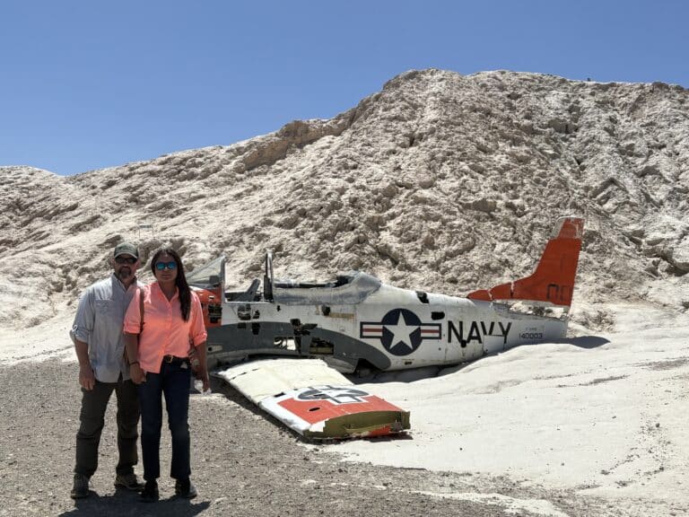 A couple in sunglasses poses by a Navy plane wreck near Las Vegas, Nevada—perfect for ATV tours and Ghost Town sightseeing.