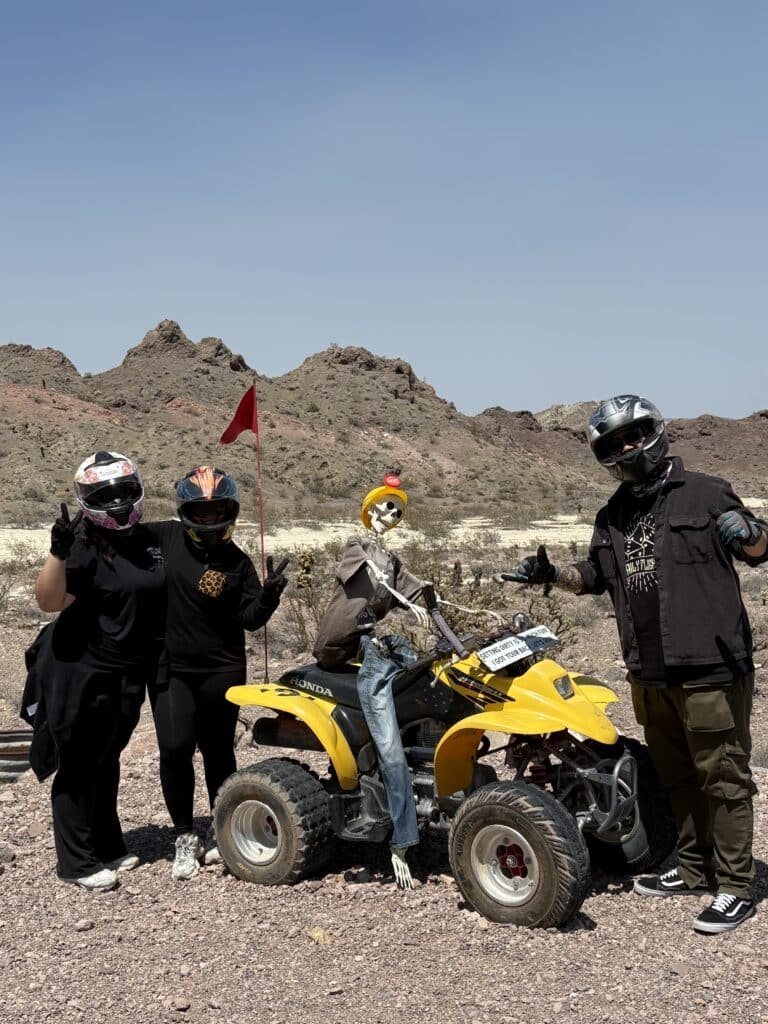 Adventurers in helmets pose by a yellow ATV with a skeleton near the Colorado River on a Nevada RZR off-road tour from Las Vegas.