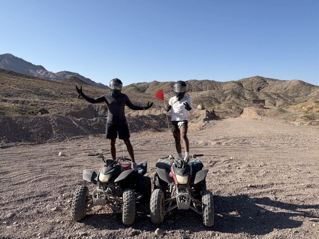 Excited riders with raised arms stand on ATVs in Nevada’s desert near Las Vegas, enjoying an adventure ATV tour.