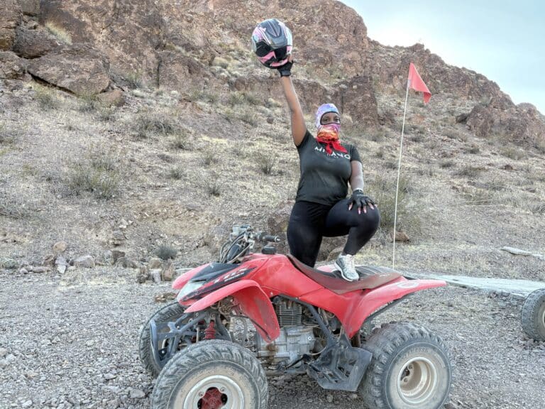 Adventurer poses with helmet on red ATV in Nevada desert near Las Vegas, ready for an epic ATV tour by the Colorado River.