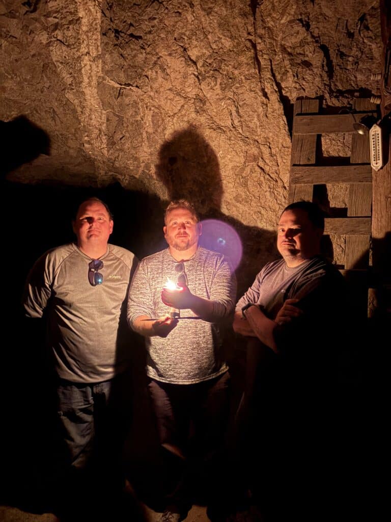 Three men explore a dim Nevada cave near the Colorado River, lit by flashlight—perfect for Las Vegas ATV or RZR ghost town tours.