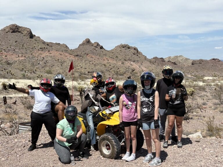 Nine adventurers in helmets pose by a yellow ATV in Nevada’s desert near Las Vegas, ready for an epic RZR off-road tour.