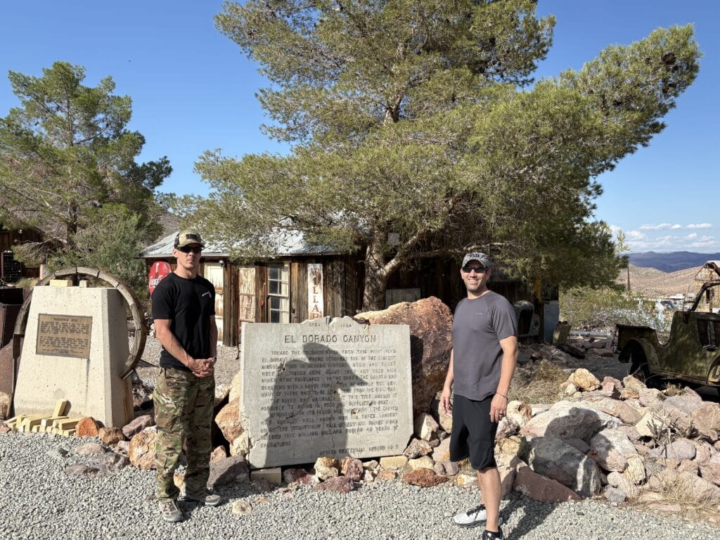 Two men pose by El Dorado Canyons historic marker near Las Vegas, Nevada—perfect for ATV tours and Ghost Town sightseeing.