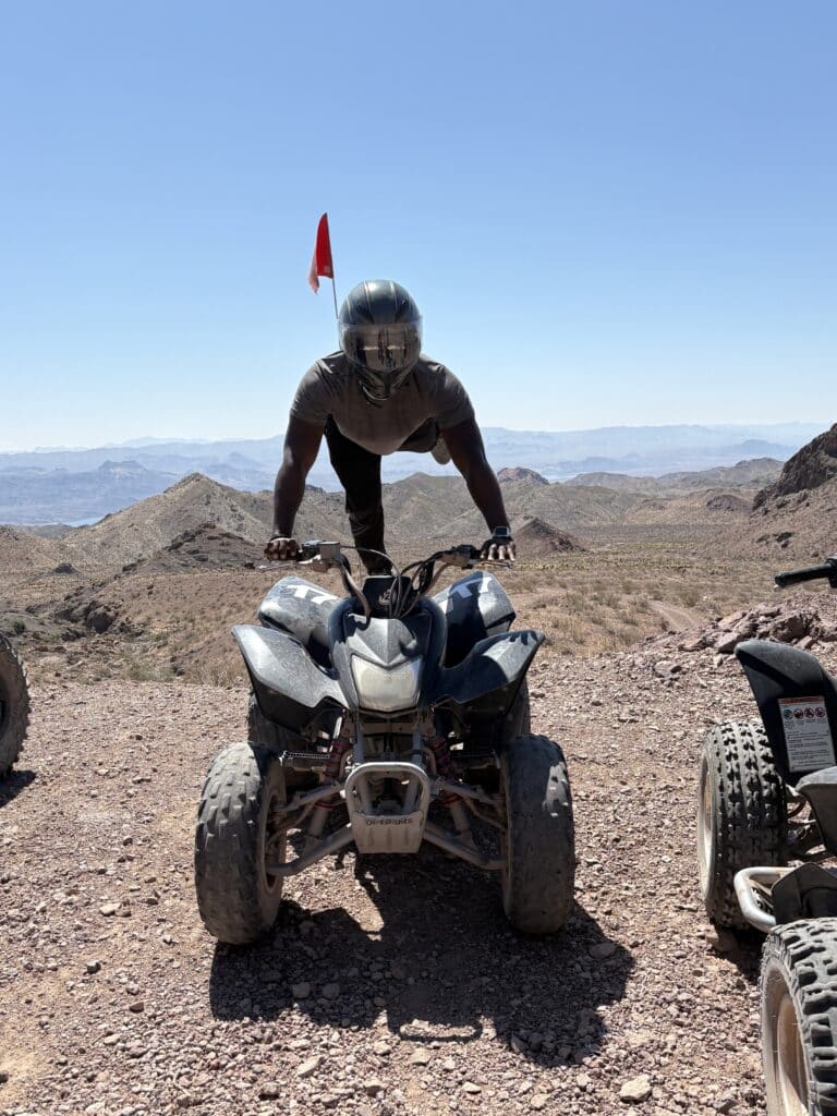 Helmeted adventurer handstands on an ATV in Nevada desert near Las Vegas on a scenic ATV tour with Colorado River views.