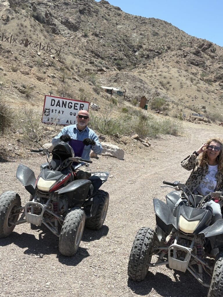 ATV riders pause on a Nevada desert trail near Las Vegas, smiling beside a Danger: Stay Out sign during an exciting RZR tour.
