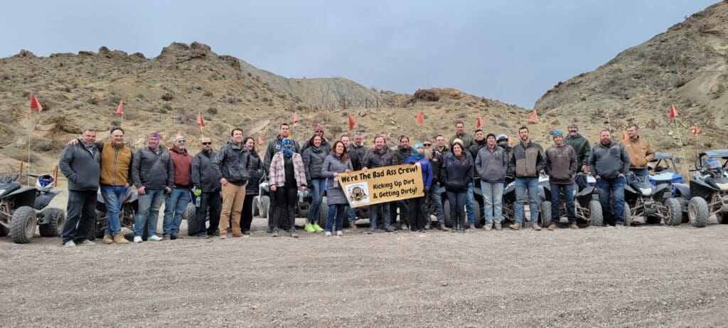 Group poses on Nevada desert rocks with “Bad Ass Fax Crew” banner, ATV & RZR tours near Las Vegas & Colorado River adventures.