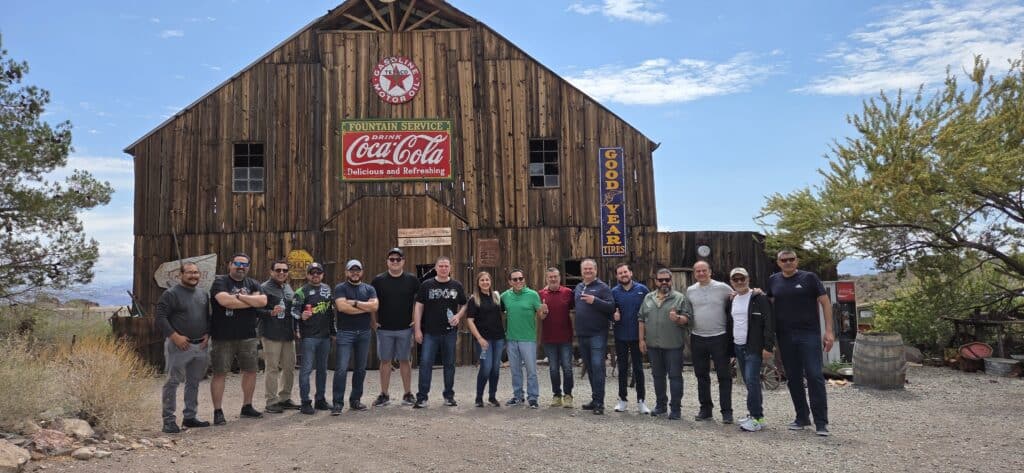 Group poses by a rustic barn with vintage signs after Las Vegas ATV tour, exploring Nevada’s Ghost Towns near the Colorado River.