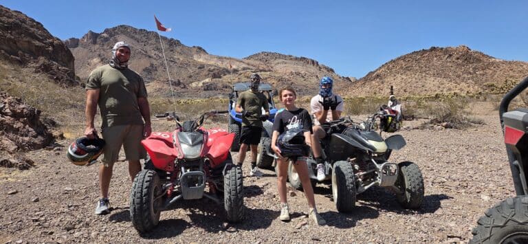 Adventure seekers in outdoor gear stand by ATVs on a Nevada desert trail near Las Vegas, ready for an epic RZR off-road tour.