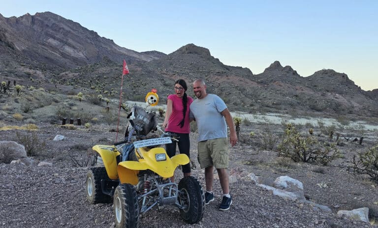 Smiling duo by a yellow ATV with skeleton rider, exploring Nevada’s rocky desert near Las Vegas on thrilling ATV tours.