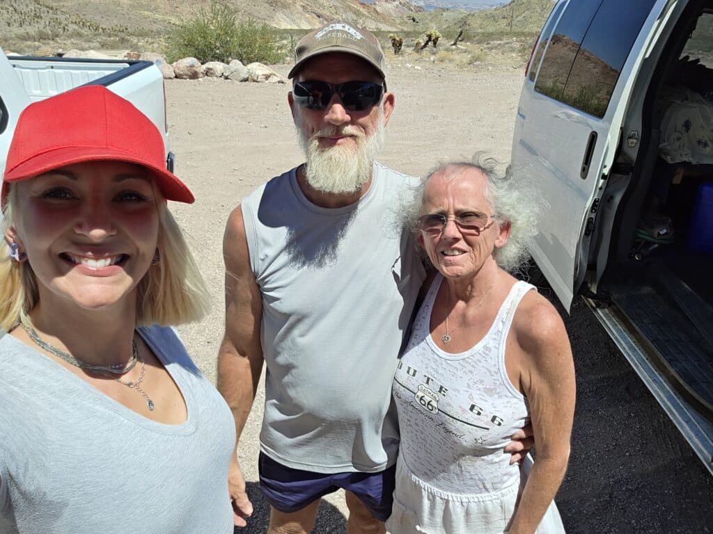 Three friends smile in sunny Nevada near Las Vegas, with a van, rocky desert views, and ready for RZR off-road adventure.