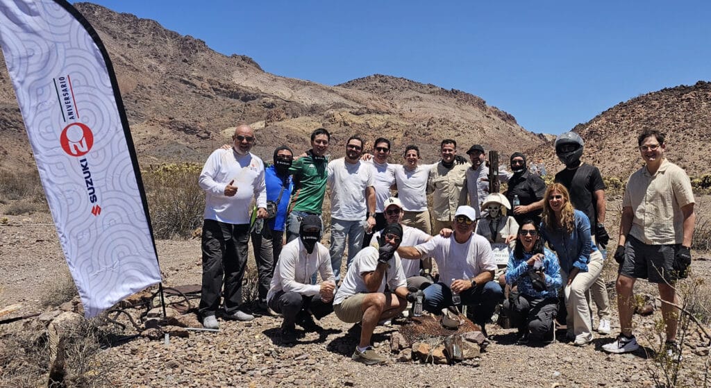 Smiling group enjoys Las Vegas ATV tour near Colorado River, Nevada desert—Suzuki banner and RZR rides in rocky landscape.