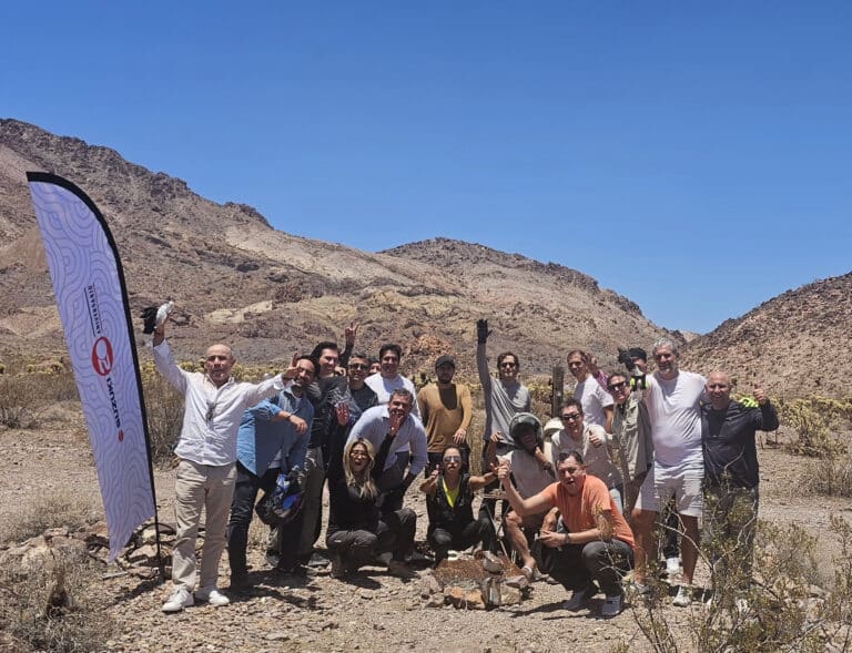 Smiling group poses in Nevada’s desert near Las Vegas, next to flag after an epic RZR off-road tour by the Colorado River.